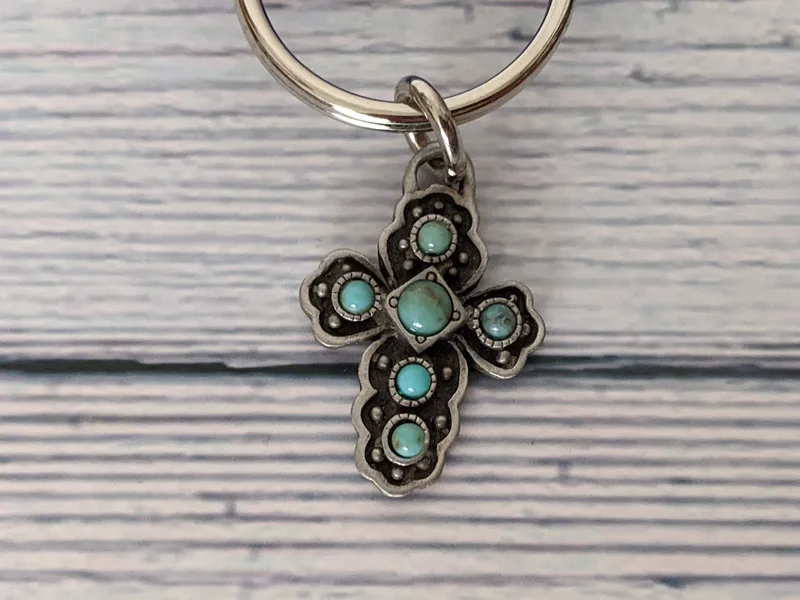 A pewter cross keyring with a pendant shaped like a cross, inlaid with faux turquoise stones.