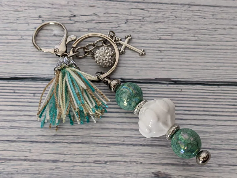 A bag charm with aqua and white beads, a matching yarn tassel, and a silver cross charm.