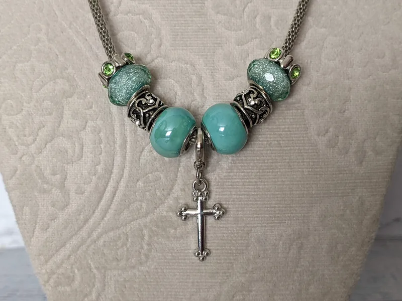 A lovely metal chain-cord necklace with aqua and silver slider beads that surround a silver cross charm.