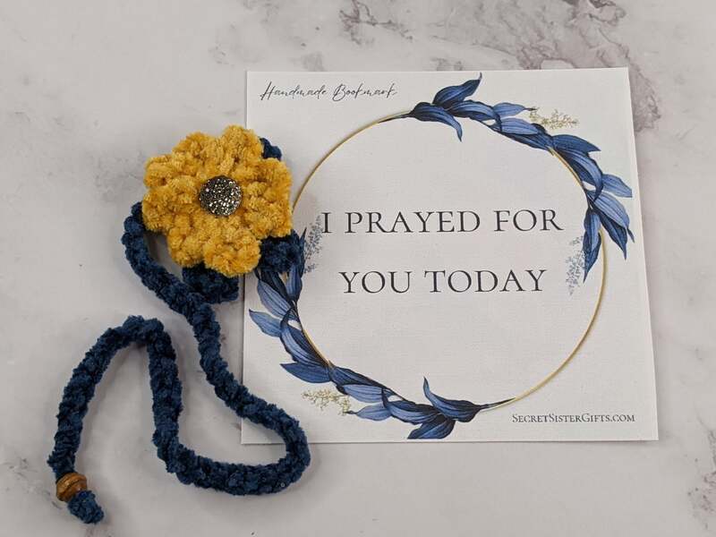 A crocheted plush yarn yellow flower bookmark with a blue strand and tassel, along with a "I prayed for you today" religious message card.