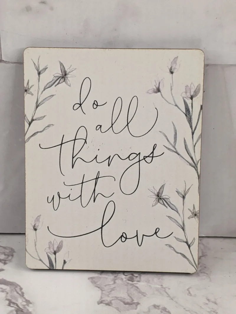 A modern white magnet with an inspirational saying, do all things with love, and a long-stemmed flower design.