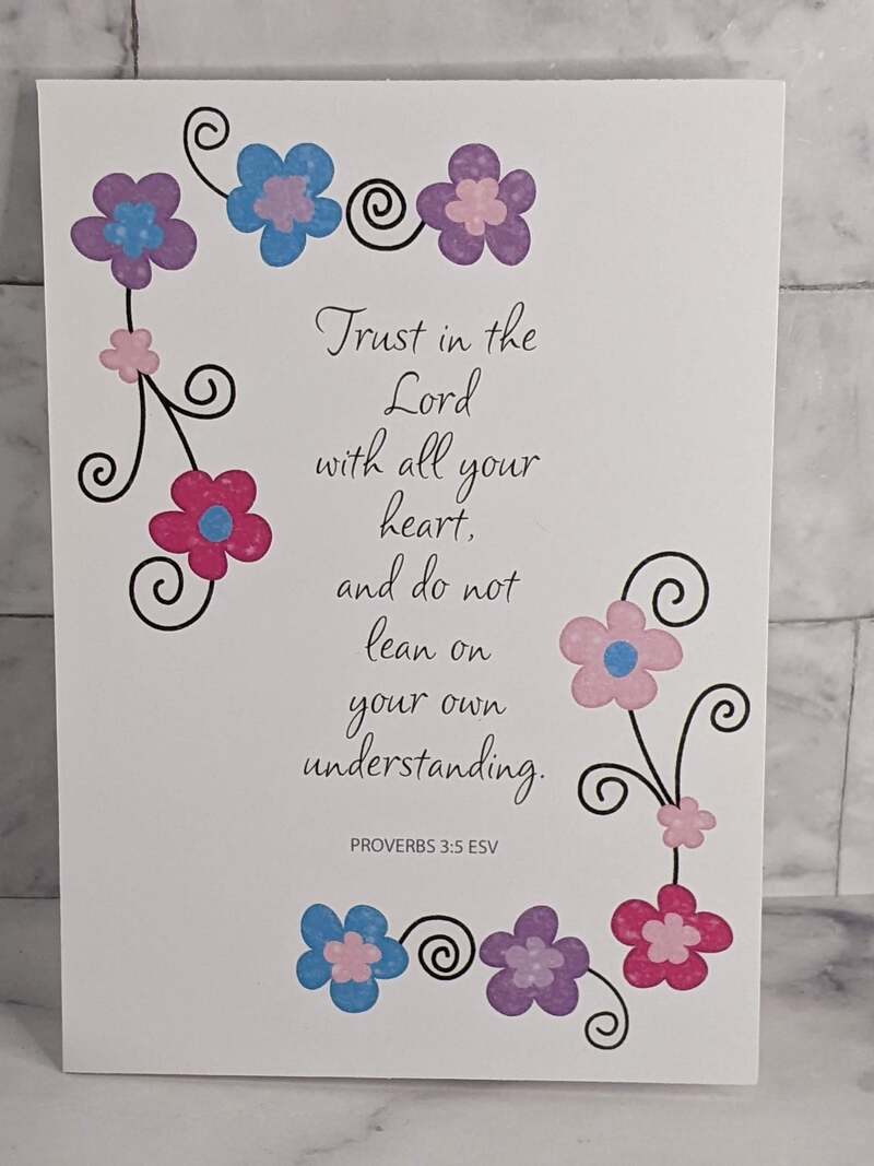 A religious greeting card with a Trust in the Lord Bible verse, and a design of pink, purple and blue flowers.