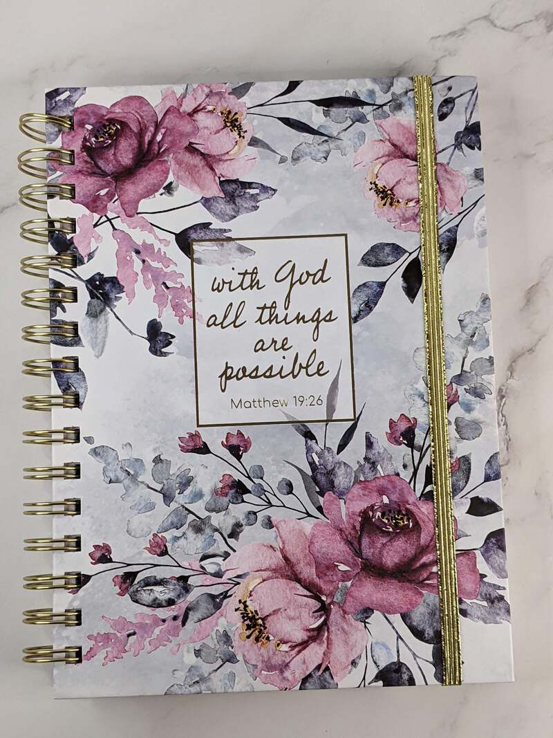 A religious spiral journal with a Bible verse on the cover, "with God all things are possible," and a purple flower design.