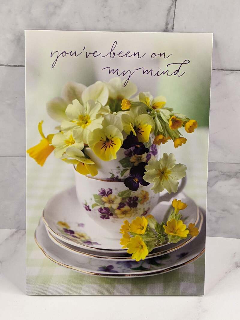 A Secret Sister greeting card with an image of a teacup with an arrangement of yellow and purple flowers.