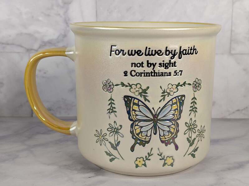 A religious gift mug with a blue butterfly design and a Bible verse about living by faith, not by sight.