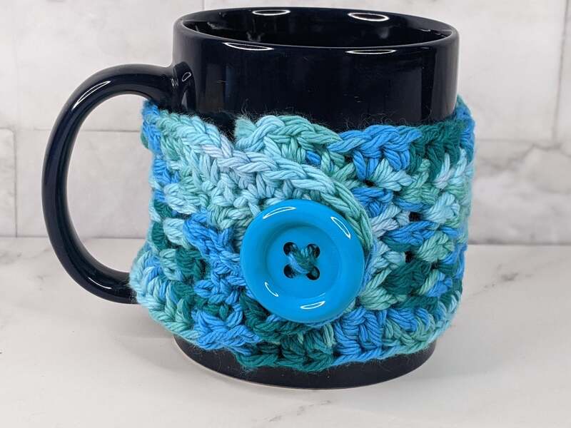 A handmade crocheted aqua blue mug cozy with a blue button closure.