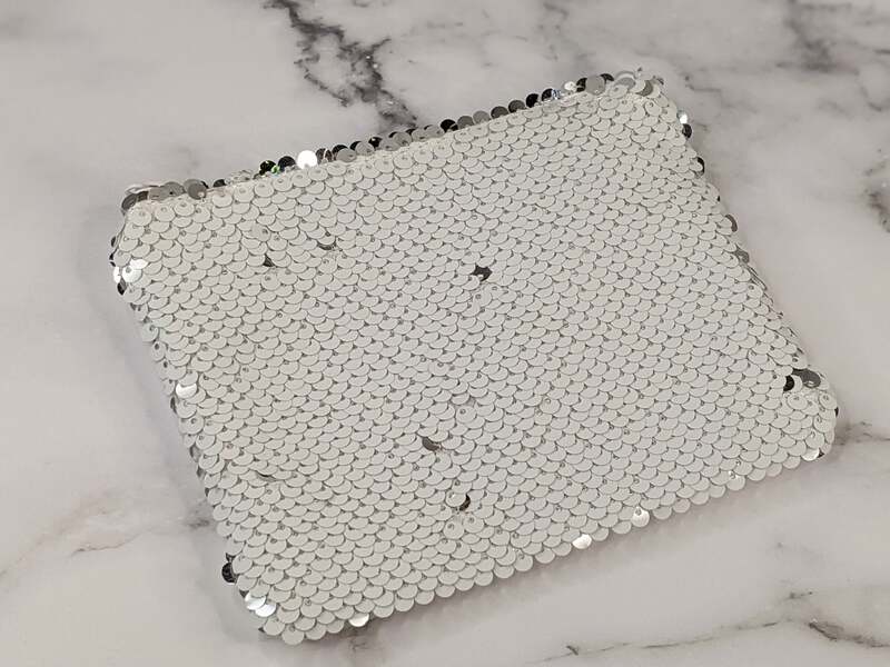 A small-zippered pouch covered in white sequins that are silver when their direction is reversed.
