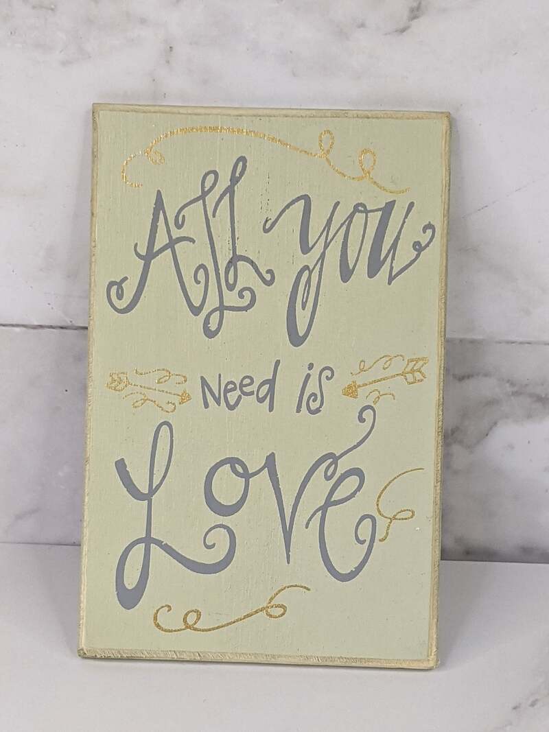 A rectangular cream-colored magnet with the words "all you need is love" in silver lettering.