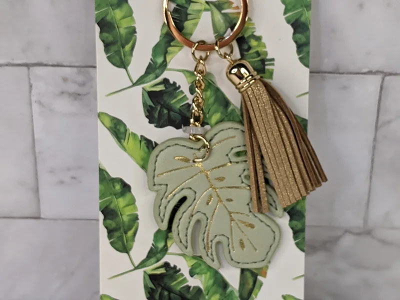 This modern trendy keyring has a leatherette green leaf motif and golden tassel.