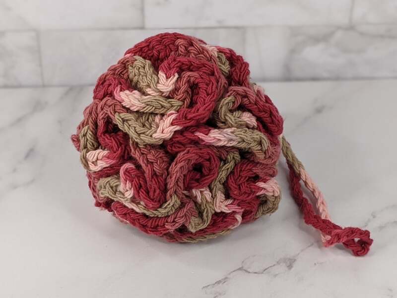 A crocheted bath sponge loofa in pink shades, made of cotton yarn.