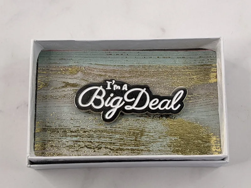 A gold lapel pin with white lettering, featuring the words "I'm a Big Deal."