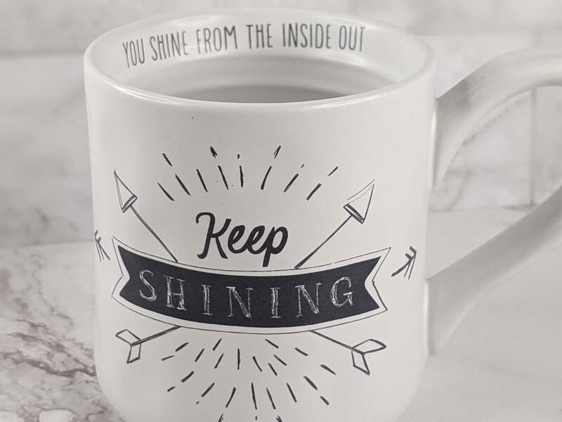 A white Scripture mug with a "Light of the World" verse, and the words "Keep Shining" in black letters.